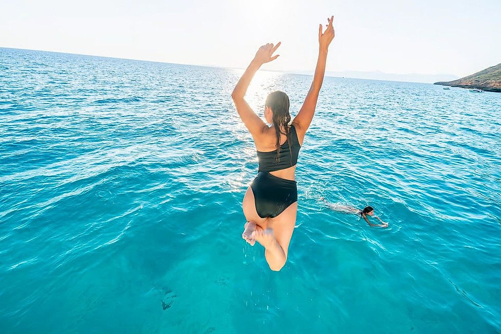Woman leaping off the boat into clear water with arms raised overhead.